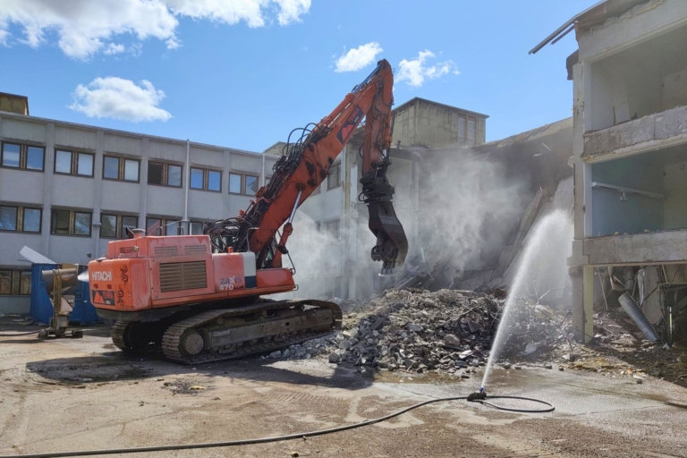 kaivinkone rakennuksen purkutöissä, vesisuihku ja betonipölyä